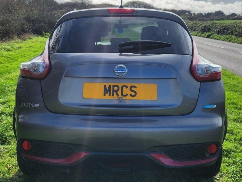 A grey and cerise Nissan Juke 1.5 dCi Acenta Premium viewed from the outside back