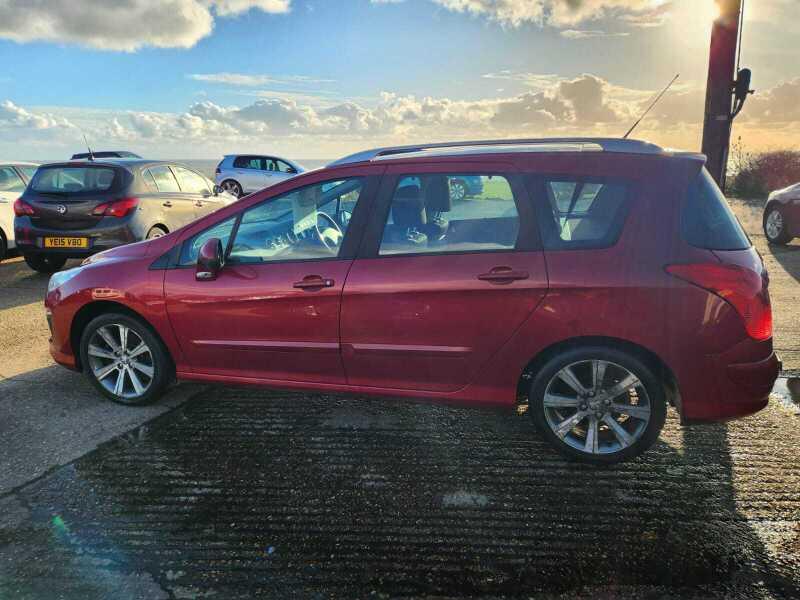 A red Peugeot 308 SW Active HDi viewed from the left side