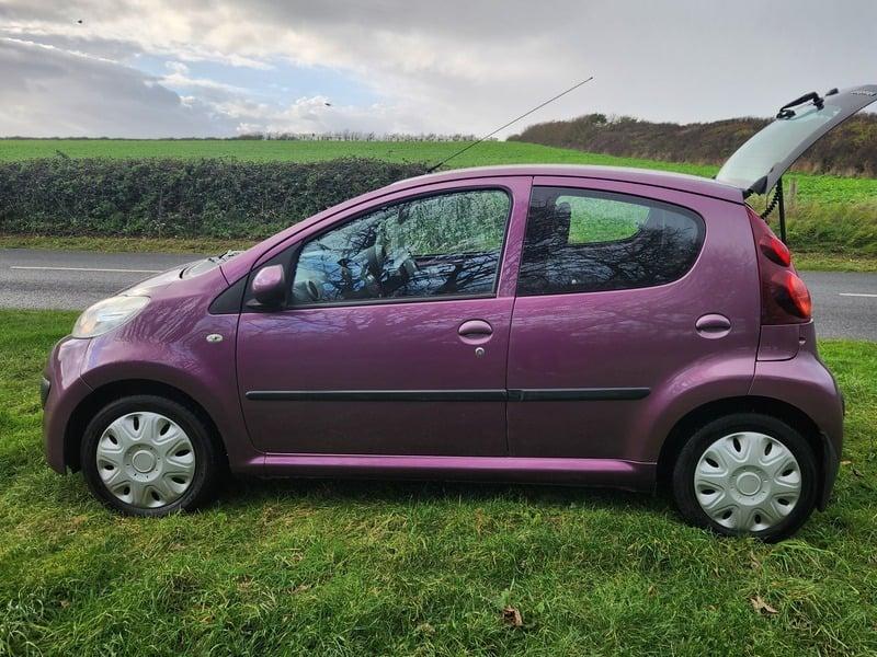 A plum purple Peugeot 107 viewed from the outside left