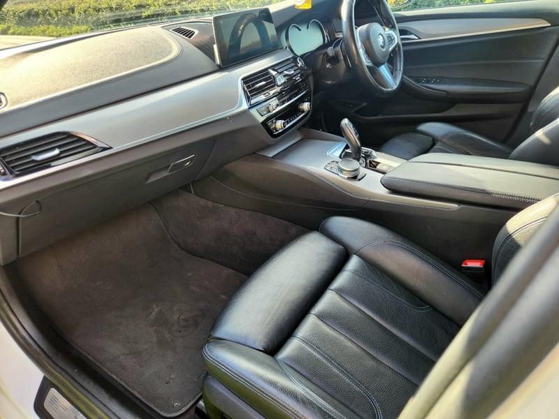 The front seats, steering wheel, and controls on a BMW 5 Series Touring 520d M Sport Auto from the passenger side