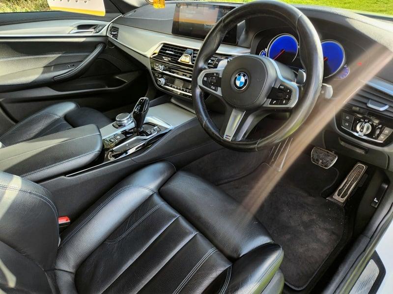 The front seats, steering wheel, and controls on a BMW 5 Series Touring 520d M Sport Auto from the right side