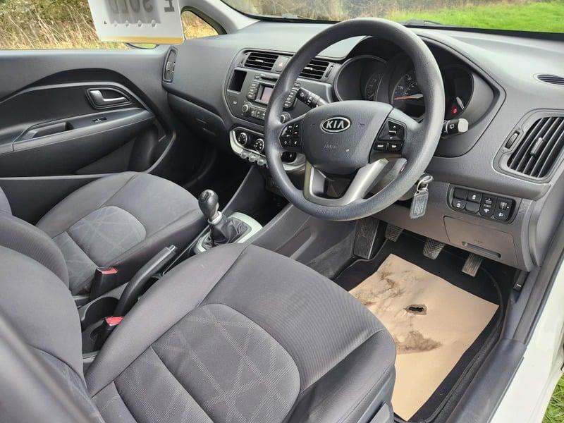The front seats, steering wheel, and controls of a white Kia Rio 1.1, viewed from the right side.