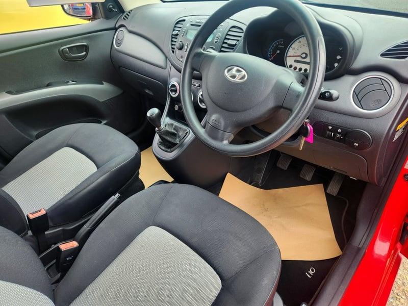 The front seats, steering wheel and controls of a bright red Hyundai i10