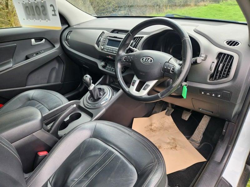 The front seats, steering wheel, and controls on a white Kia Rio Sportage 2.0 CRDi KX-3, viewed from the right side.