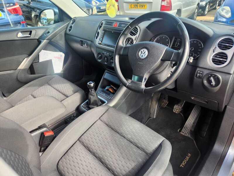 The front seats, steering wheel, and controls on a grey Volkswagen Tiguan, viewed from the right side.
