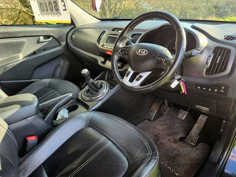 The front seats, steering wheel, and controls on a black Kia Sportage 2.0, viewed from the right side.