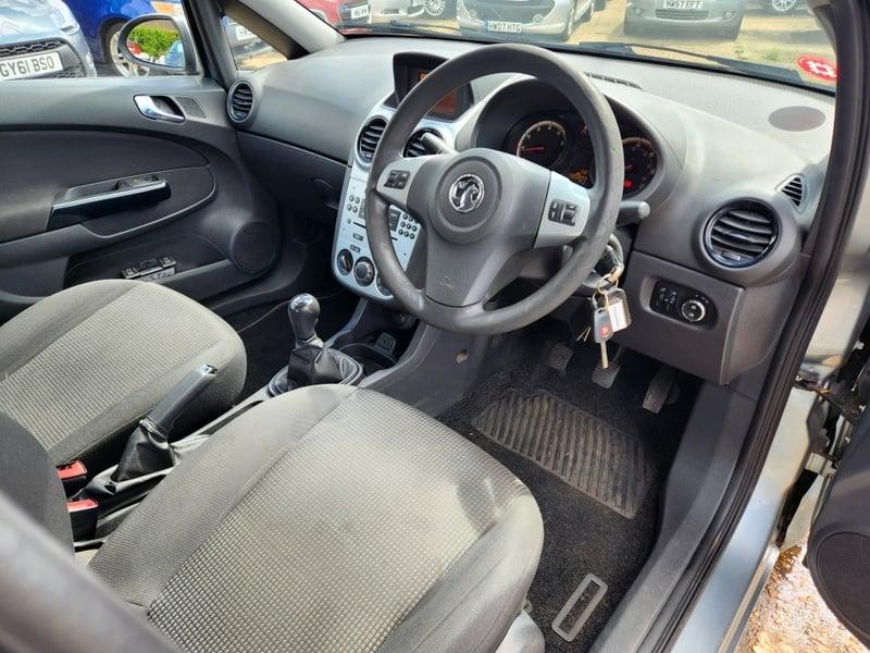 The front seats, steering wheel, and controls on a silver Vauxhall Corsa Excite, viewed from the right side.