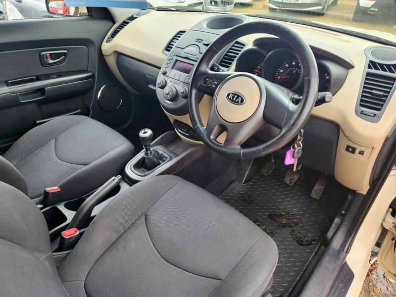 The front seats, steering wheel, and controls on a white Kia Soul MPV, viewed from the right side.