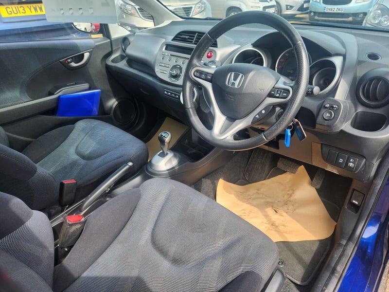 The front seats, steering wheel, and controls on a blue Honda Jazz, viewed from the right side.