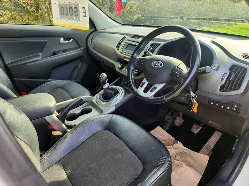 The front seats, steering wheel, and controls on a white Kia Sportage 1.6 GDi 2, viewed from the right side.