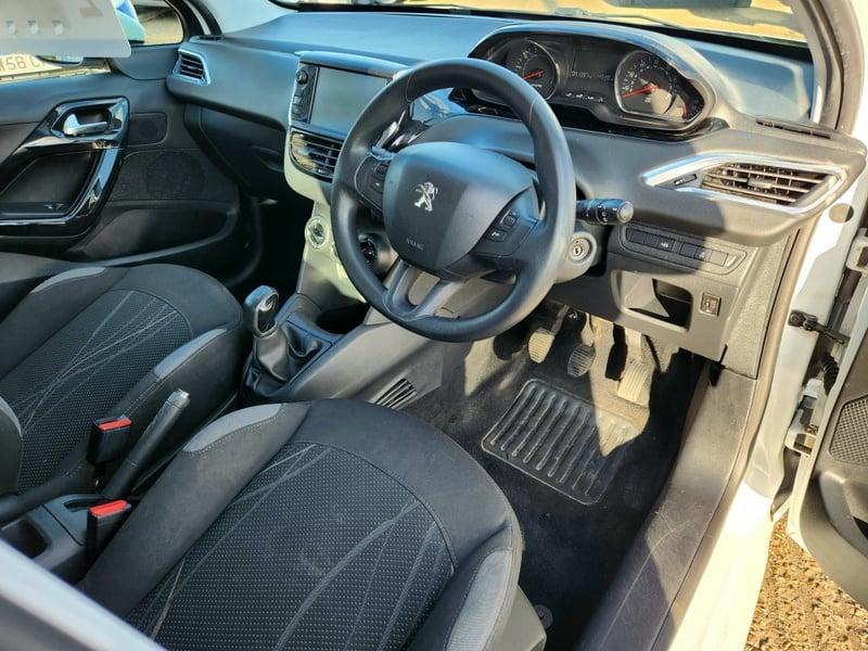 The front seats, steering wheel, and controls on a Bright White Peugeot 208 Active, viewed from the right side.