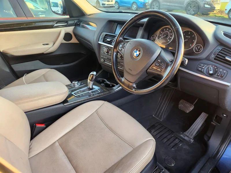 The front seats and driver controls of a Deepsea Blue BMW X3 viewed from the driver's side