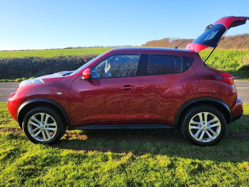 A cayenne red Nissan Juke Acente viewed from the passenger side
