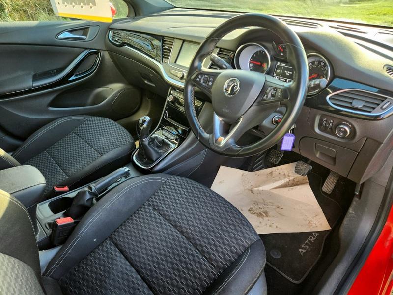 The steering wheel and controls of a Power Red Vauxhall Astra viewed from the driver's seat