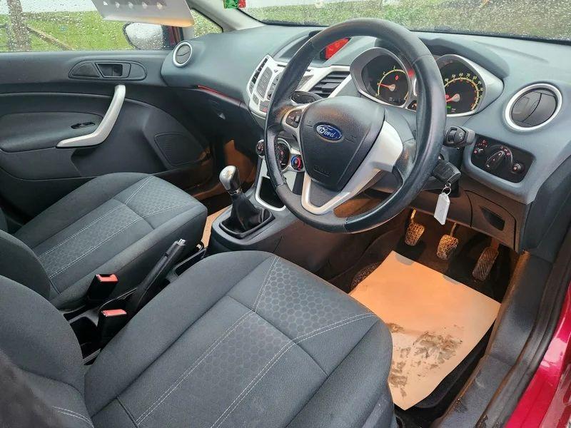 The steering controls of a Burgundy Ford Fiesta viewed from above the driver seat