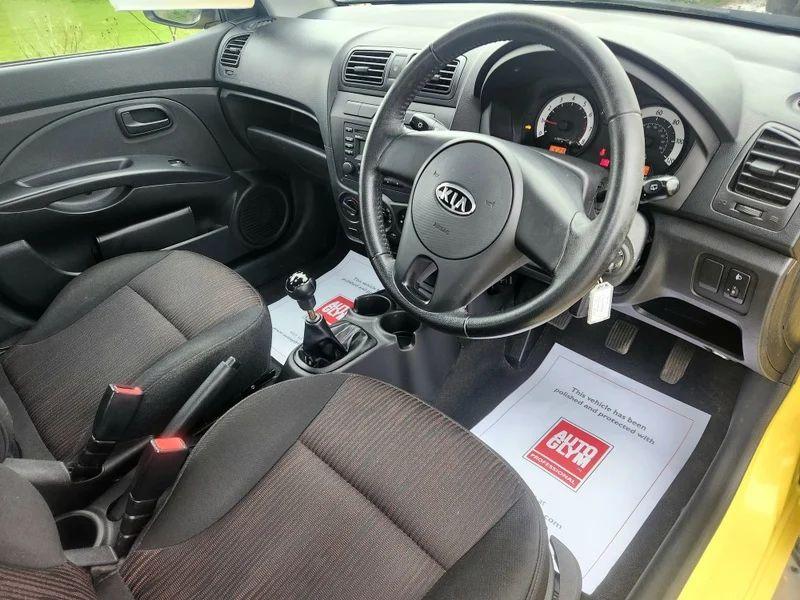 The steering controls of a yellow KIA Picanto viewed from above the driver seat