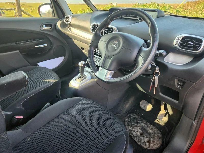 The steering controls of a red Citroen Picasso viewed from above the driver seat