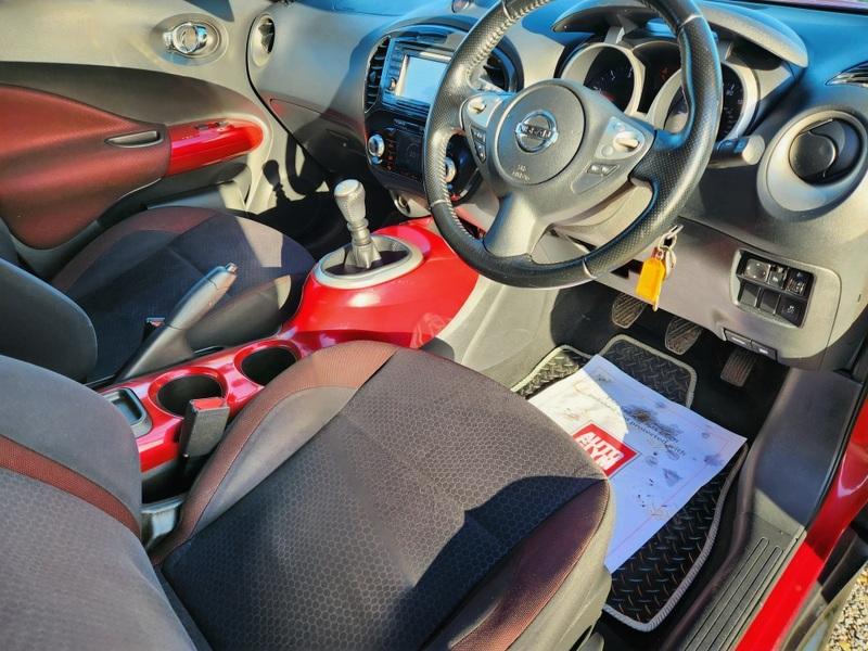 The steering controls of a red Nissan Juke Acenta viewed from above the driver seat