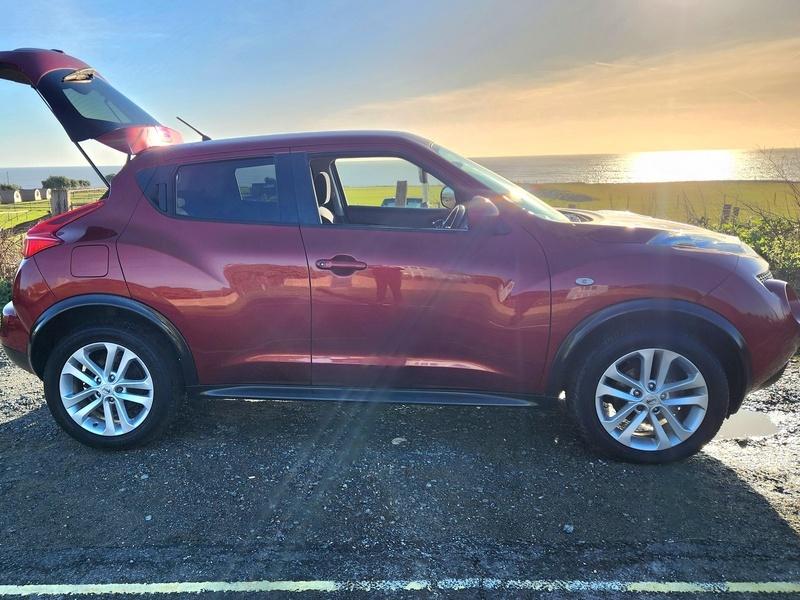 A red Nissan Juke Acenta viewed from the driver side