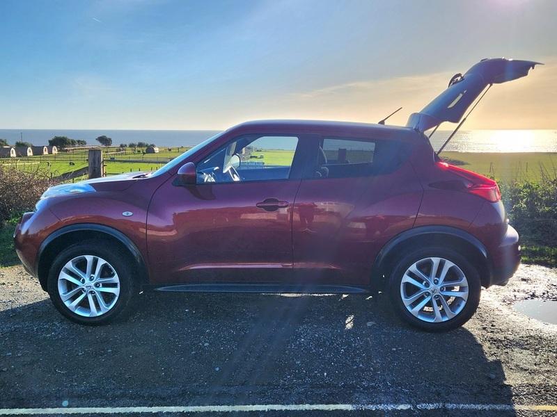A red Nissan Juke Acenta viewed from the passenger side