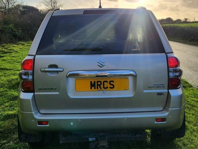 A Suzuki Grand Vitara in Mars Gold Metallic, viewed from the back.