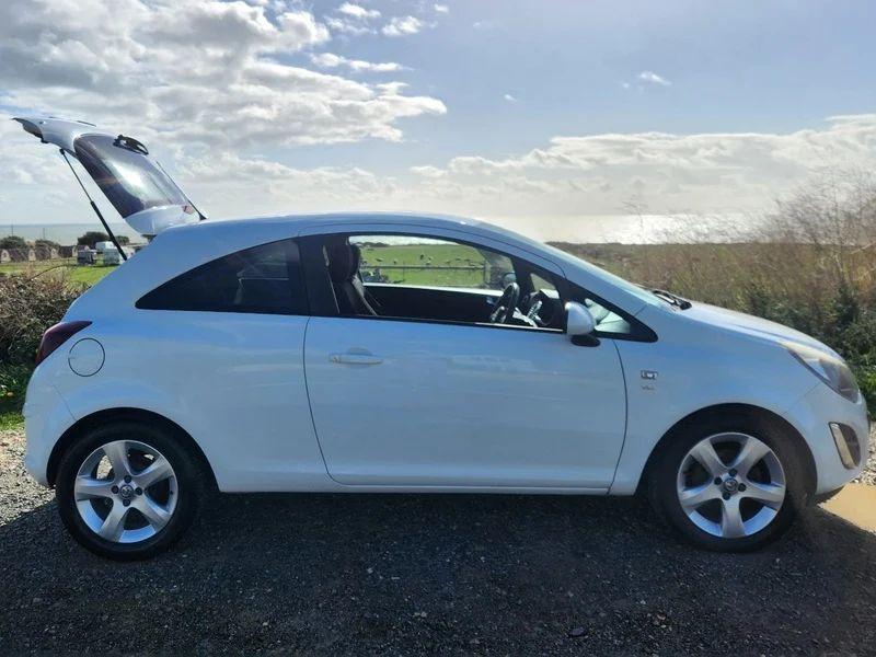 A Snow White Vauxhall Corsa with an open boot viewed from the driver side